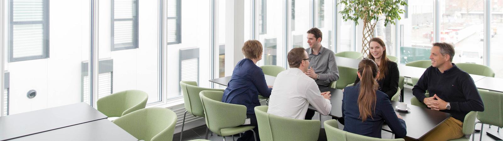 Sechs Personen sitzen an Tisch und unterhalten sich.